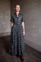 Image of model wearing Trovata Martine cotton dress in  a dark floral print with ruffle trim short sleeves