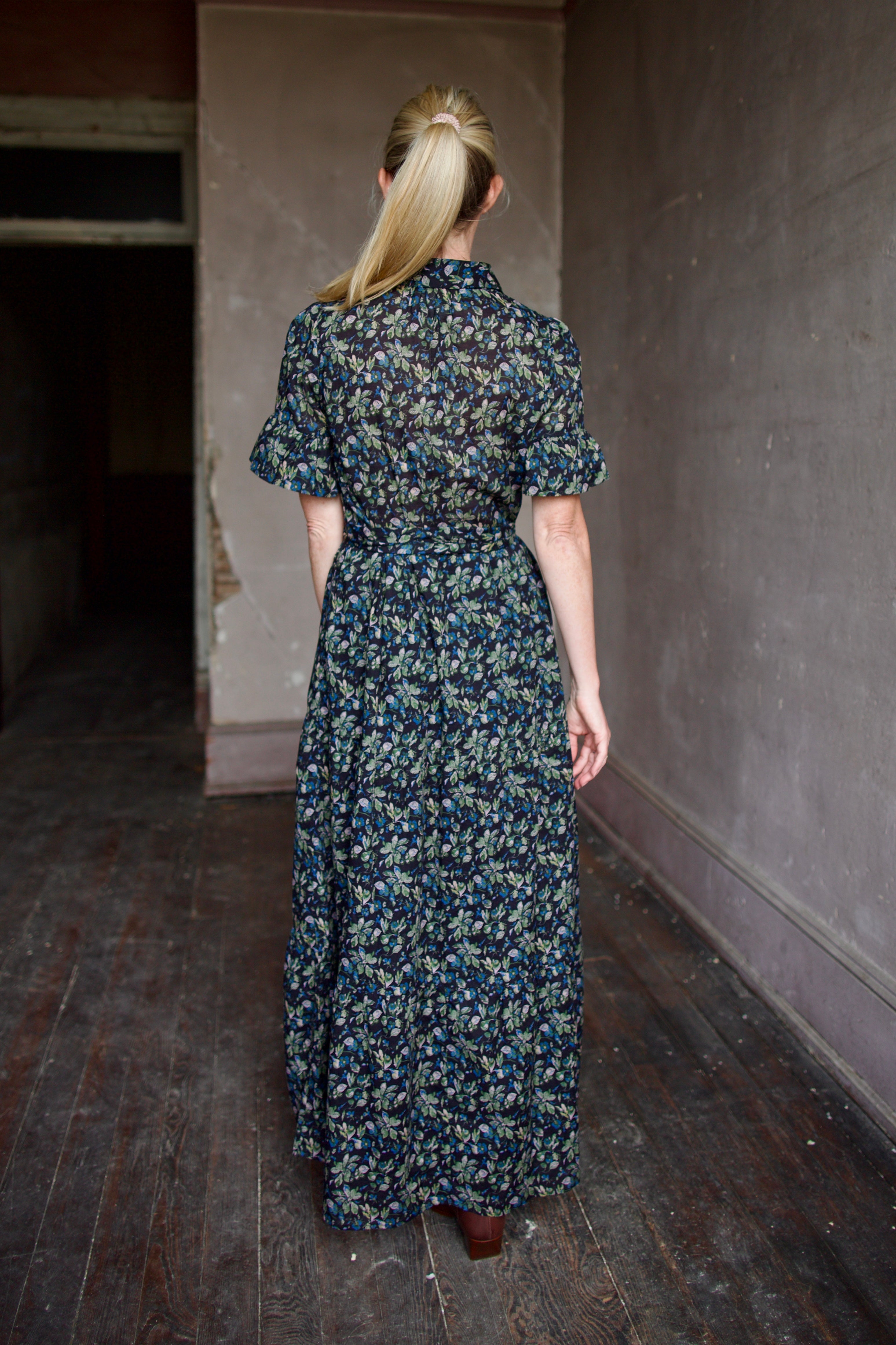 Back of model wearing Trovata Martine cotton dress in  a dark floral print with ruffle trim short sleeves