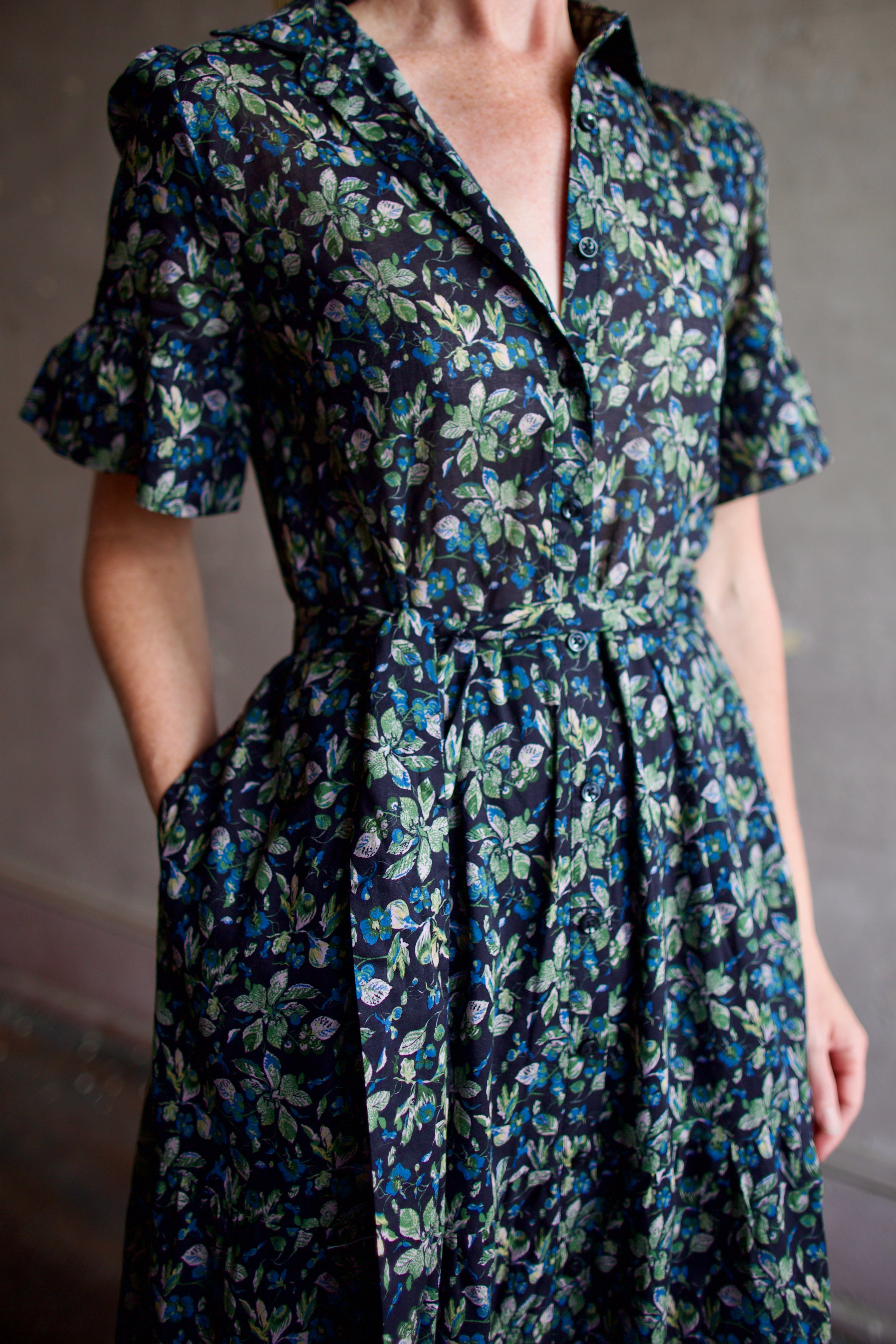 Image of model wearing Trovata Martine cotton dress in  a dark floral print with ruffle trim short sleeves