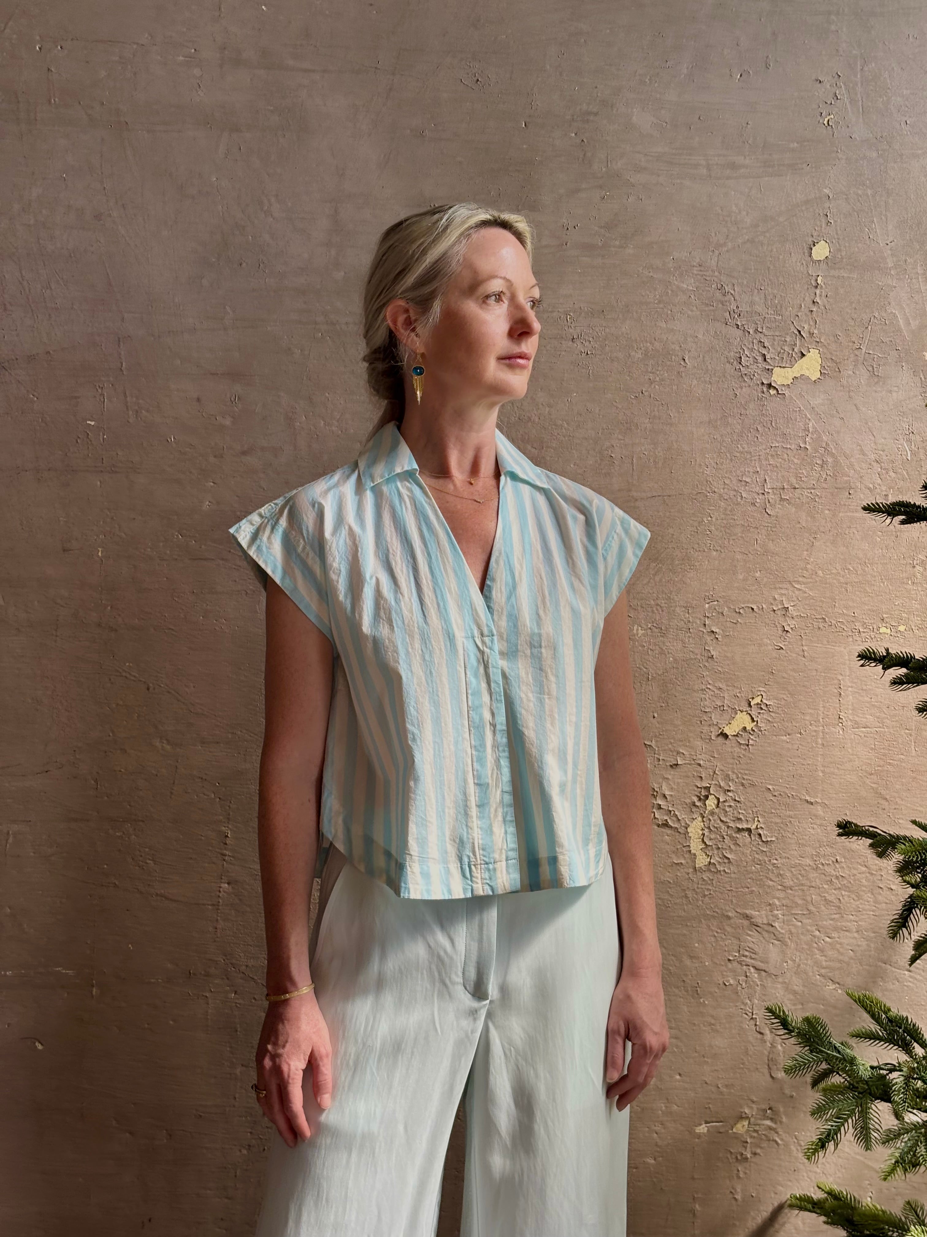 Mature woman wearing Dorada short sleeve Shirt from Trovata rendered in a fresh aqua and cream Stripe and crafted from  cotton poplin with v-neck, collar and consealed button front