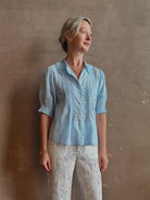 Mature woman wearing Jess Blouse from Trovata rendered in the light blur and crafted from cotton poplin with peter pan collar, half sleeves, intricate pitucking and button front