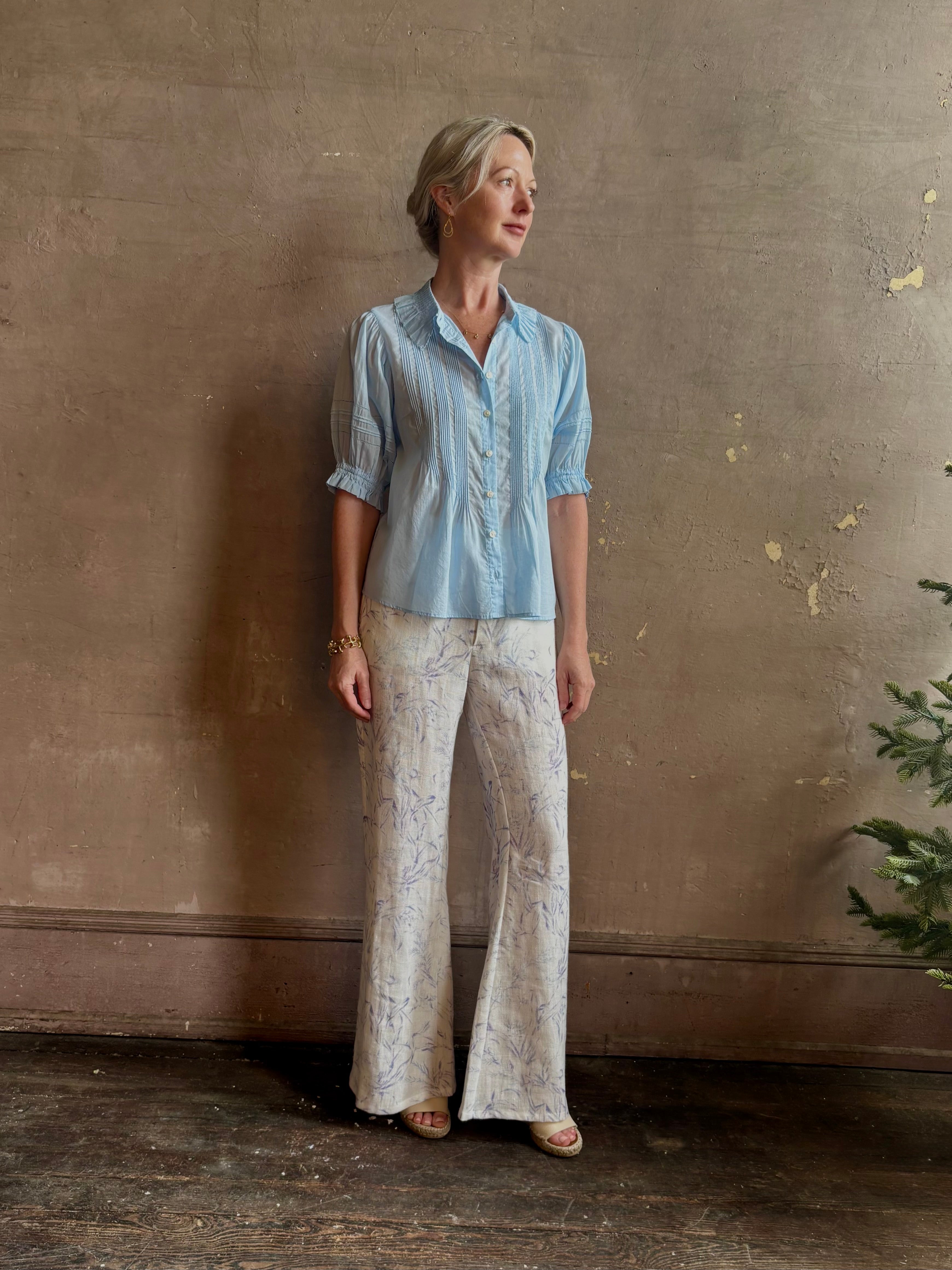 Mature woman wearing Jess Blouse from Trovata rendered in the light blur and crafted from cotton poplin with peter pan collar, half sleeves, intricate pitucking and button front
