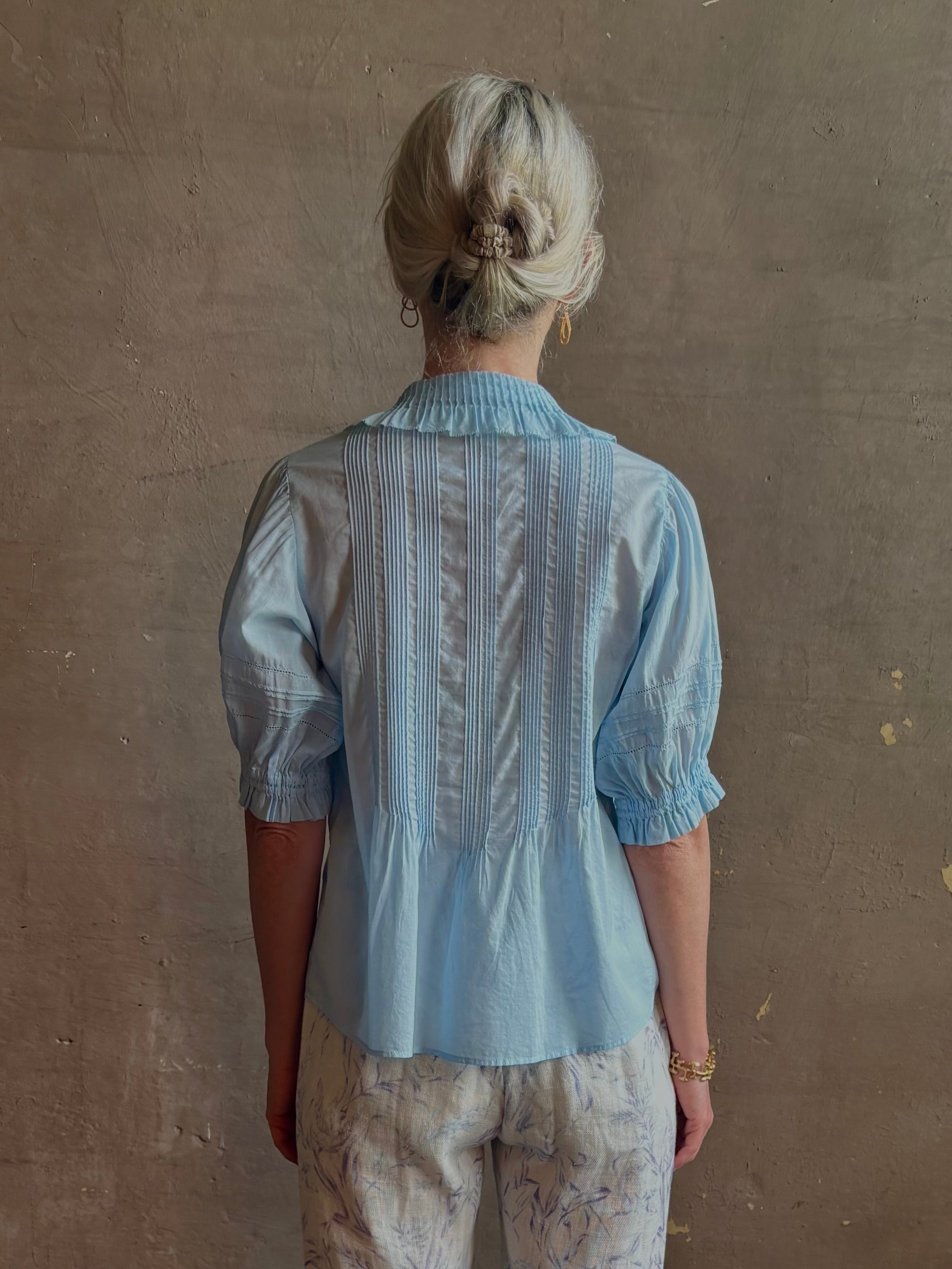 Mature woman wearing Jess Blouse from Trovata rendered in the light blur and crafted from cotton poplin with peter pan collar, half sleeves, intricate pitucking and button front