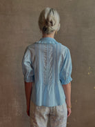 Mature woman wearing Jess Blouse from Trovata rendered in the light blur and crafted from cotton poplin with peter pan collar, half sleeves, intricate pitucking and button front