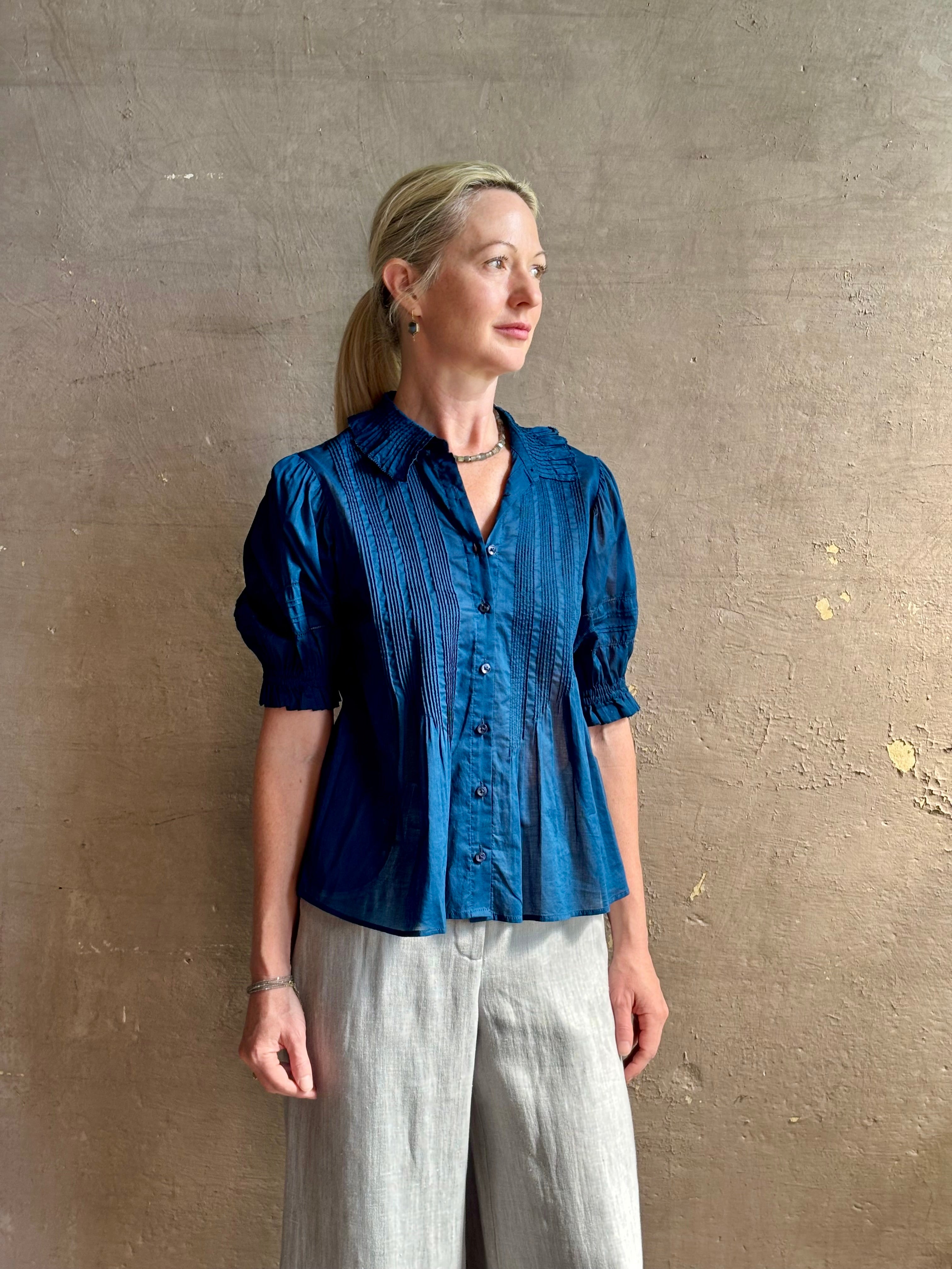 Mature woman wearing Jess Blouse from Trovata rendered in a classic  Navy blue and crafted from light weight cotton poplin with short sleeves, peter pan collar, v-neck button front with intricate pintucking details at front and back