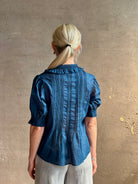 Mature woman wearing Jess Blouse from Trovata rendered in a classic  Navy blue and crafted from light weight cotton poplin with short sleeves, peter pan collar, v-neck button front with intricate pintucking details at front and back