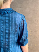 Mature woman wearing Jess Blouse from Trovata rendered in a classic  Navy blue and crafted from light weight cotton poplin with short sleeves, peter pan collar, v-neck button front with intricate pintucking details at front and back
