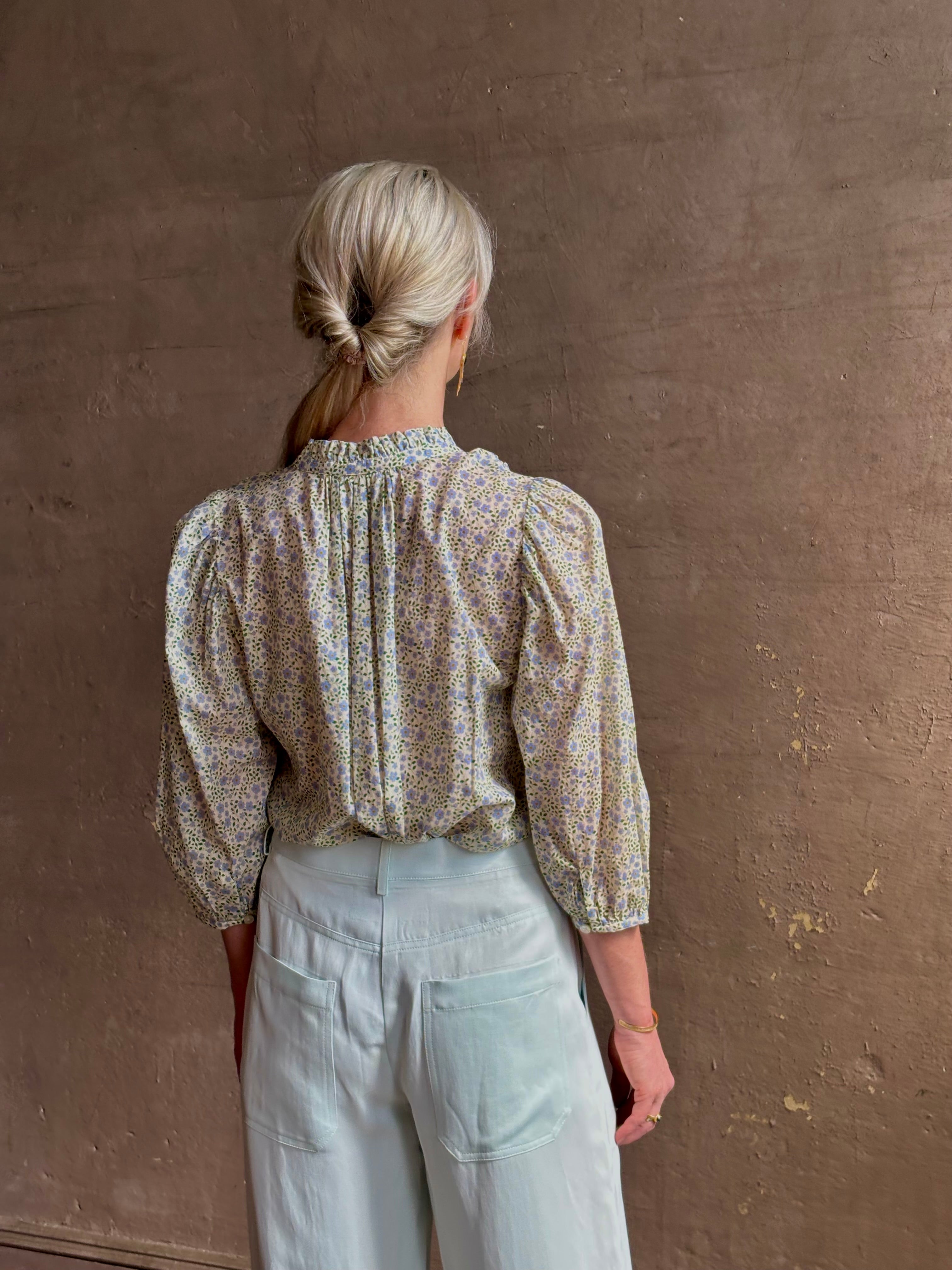 Mature woman wearing the Orly blouse from Trovata rendered in a charming coastal inspired floral print and crafted from cotton with three quarter sleeves and ruffle lined v-neck
