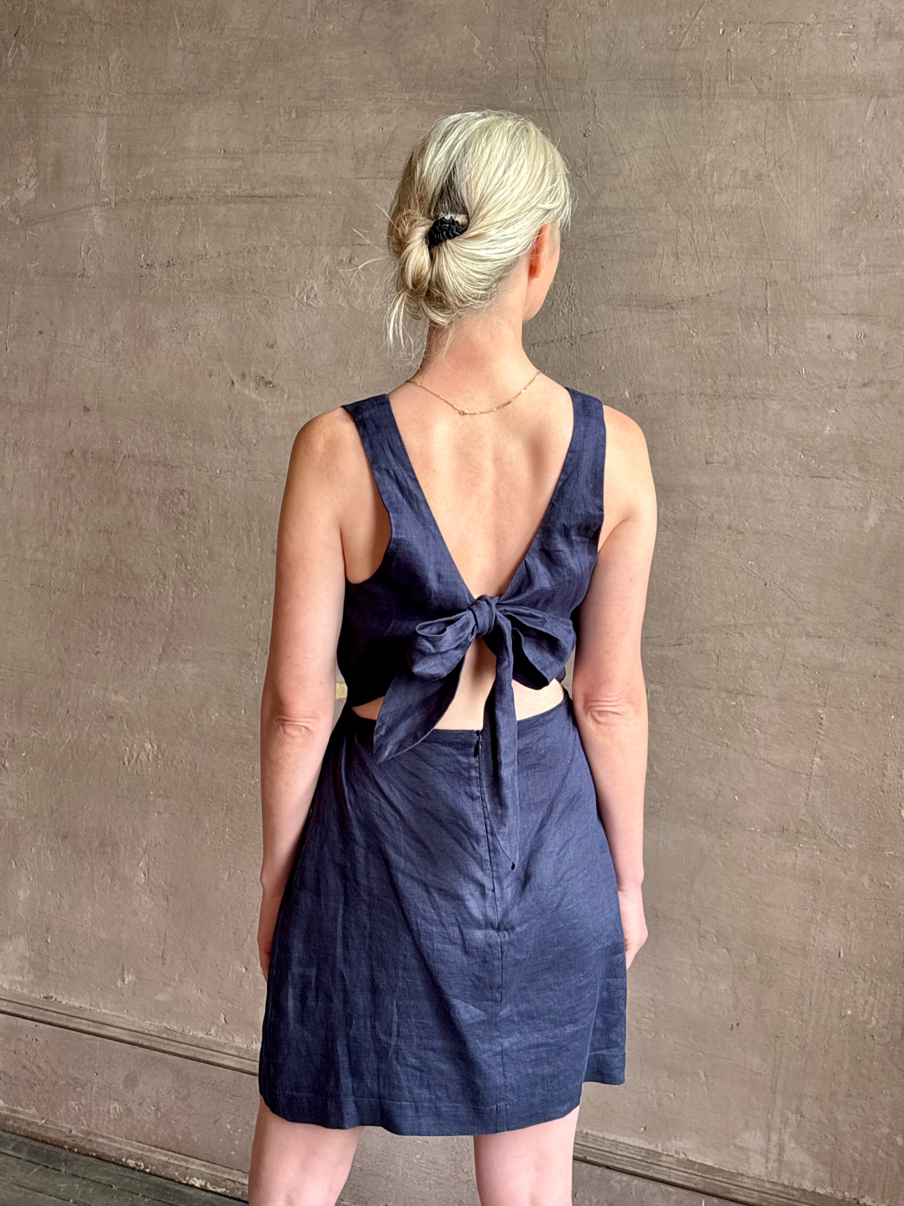 Woman wearing the effortless summer dress by Trovata Rosalie linen Dress in Navy Blue with A-line skirt and sophisticated bra friendly open back