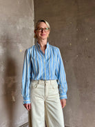 Mature woman in Trovata Rumi blue and cream vertically striped long-sleeve cotton shirt ruffle lined mandarin collar