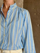 Mature woman wearing blue and cream vertically striped long-sleeve cotton Trovata Rumi shirt ruffle lined mandarin collar