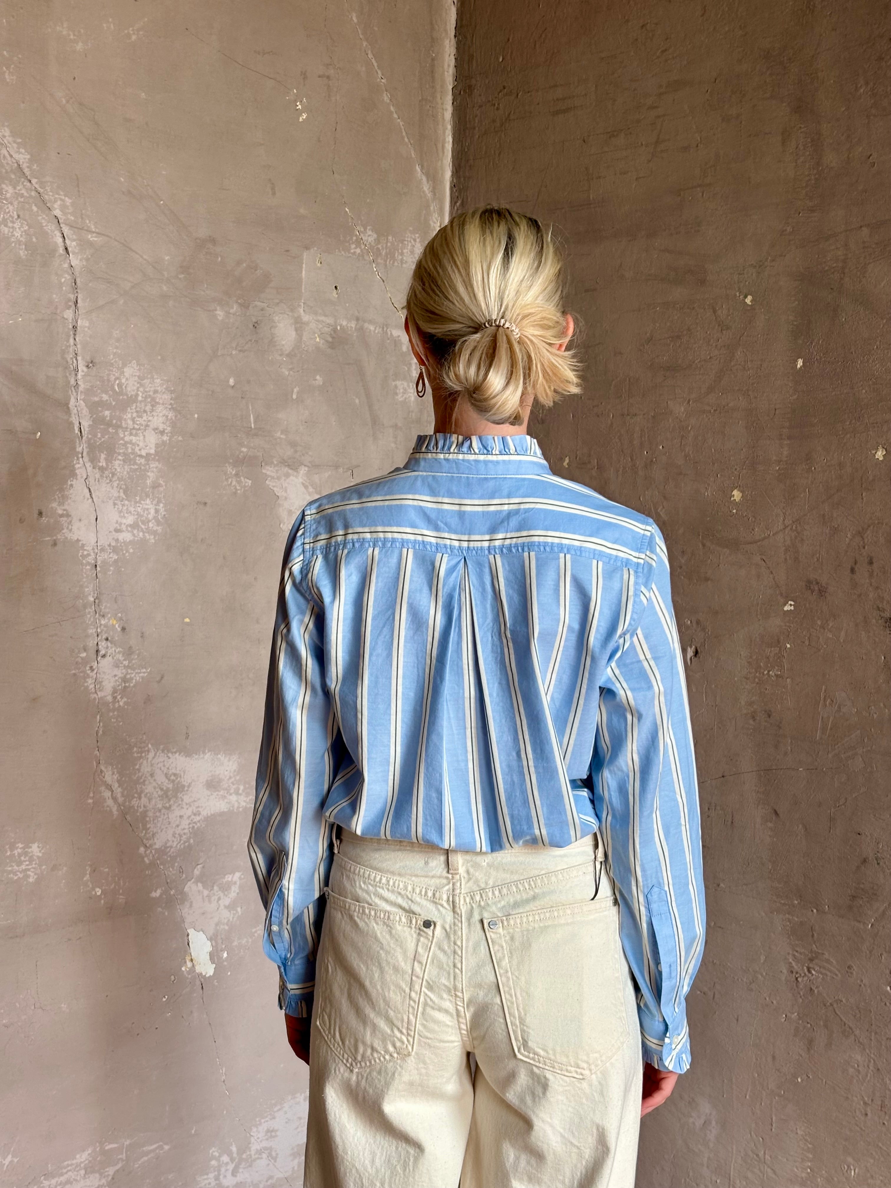 Mature woman wearing blue and cream vertically striped long-sleeve cotton Trovata Rumi shirt ruffle lined cuffs