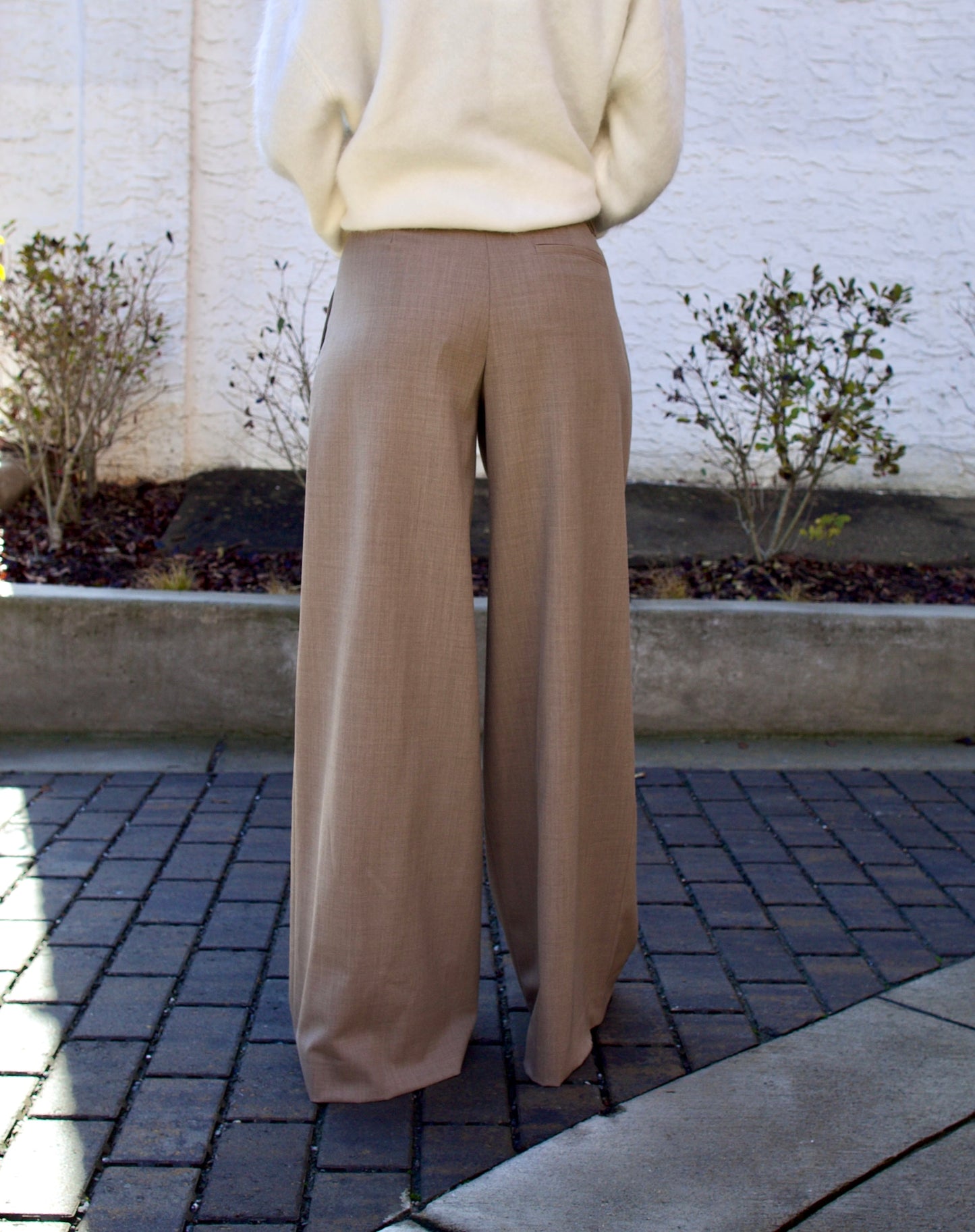 Image of the back of a woman wearing the TWP new didi pants in sandstone, the Ulla Johnson gia belt, and the Lisa Yang Margareta sweater.