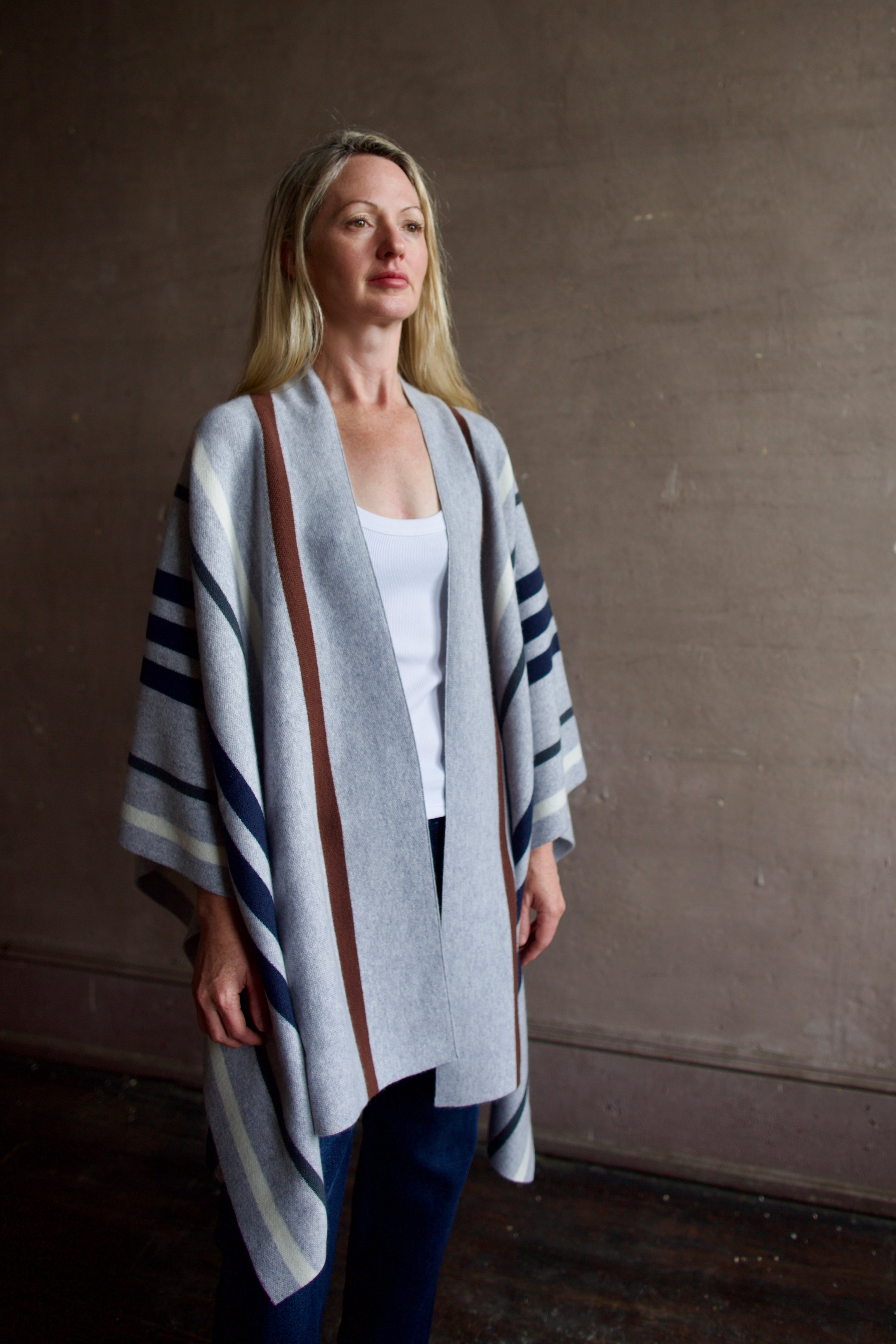 Mature Model wearing gray TWP luxury Italian cashmere poncho with brown and navy stripes and dark denim