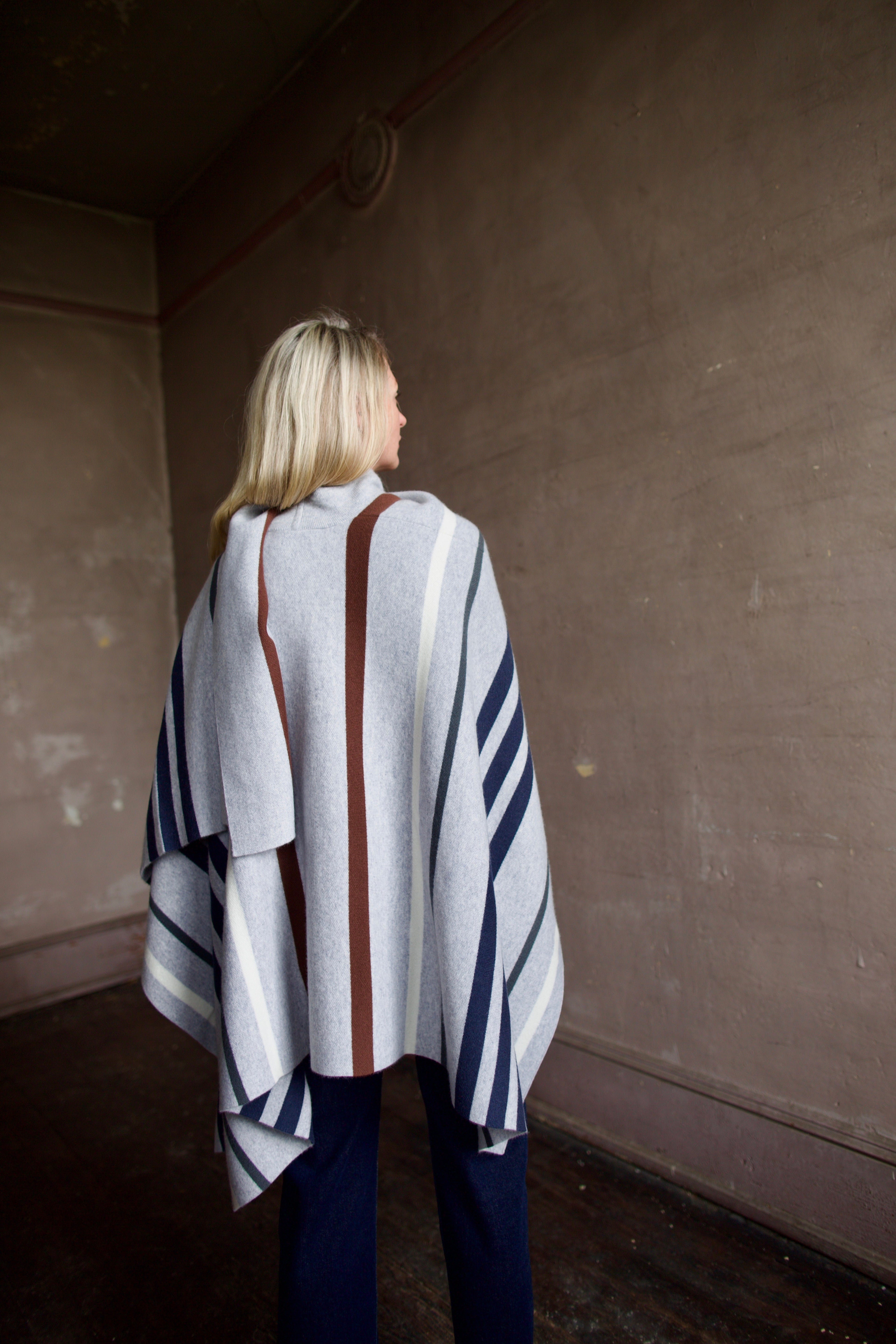 Mature Model wearing gray TWP luxury Italian cashmere poncho with brown and navy stripes 
