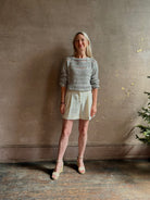 Mature woman wearing elevated tailored Cisco Shorts from TWP rendered in a soft bone white and crafted in the USA using a viscose and  linen blend fabric with side seam pockets, belt loops, single front pleat and cuffed at the bottom