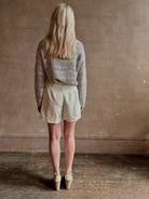 Mature woman wearing elevated tailored Cisco Shorts from TWP rendered in a soft bone white and crafted in the USA using a viscose and  linen blend fabric with side seam pockets, belt loops, single front pleat and cuffed at the bottom