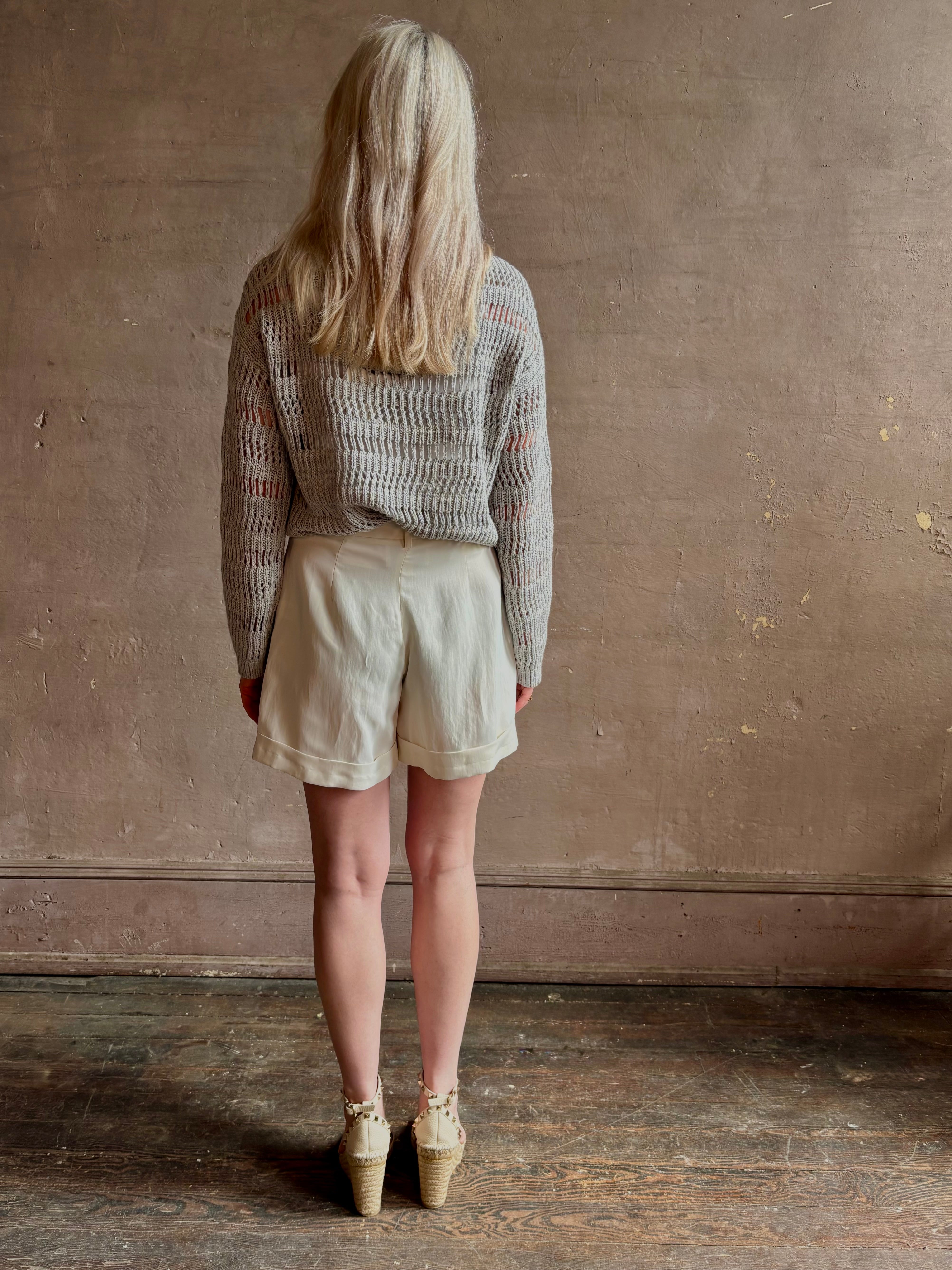 Mature woman wearing elevated tailored Cisco Shorts from TWP rendered in a soft bone white and crafted in the USA using a viscose and  linen blend fabric with side seam pockets, belt loops, single front pleat and cuffed at the bottom