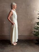Mature woman wearing elegant Crew Neck maxi A-Line Dress with Darts from TWP rendered in a soft off white and crafted in the USA from a viscose and linen fabric blend with side seam pockets and sleeveless