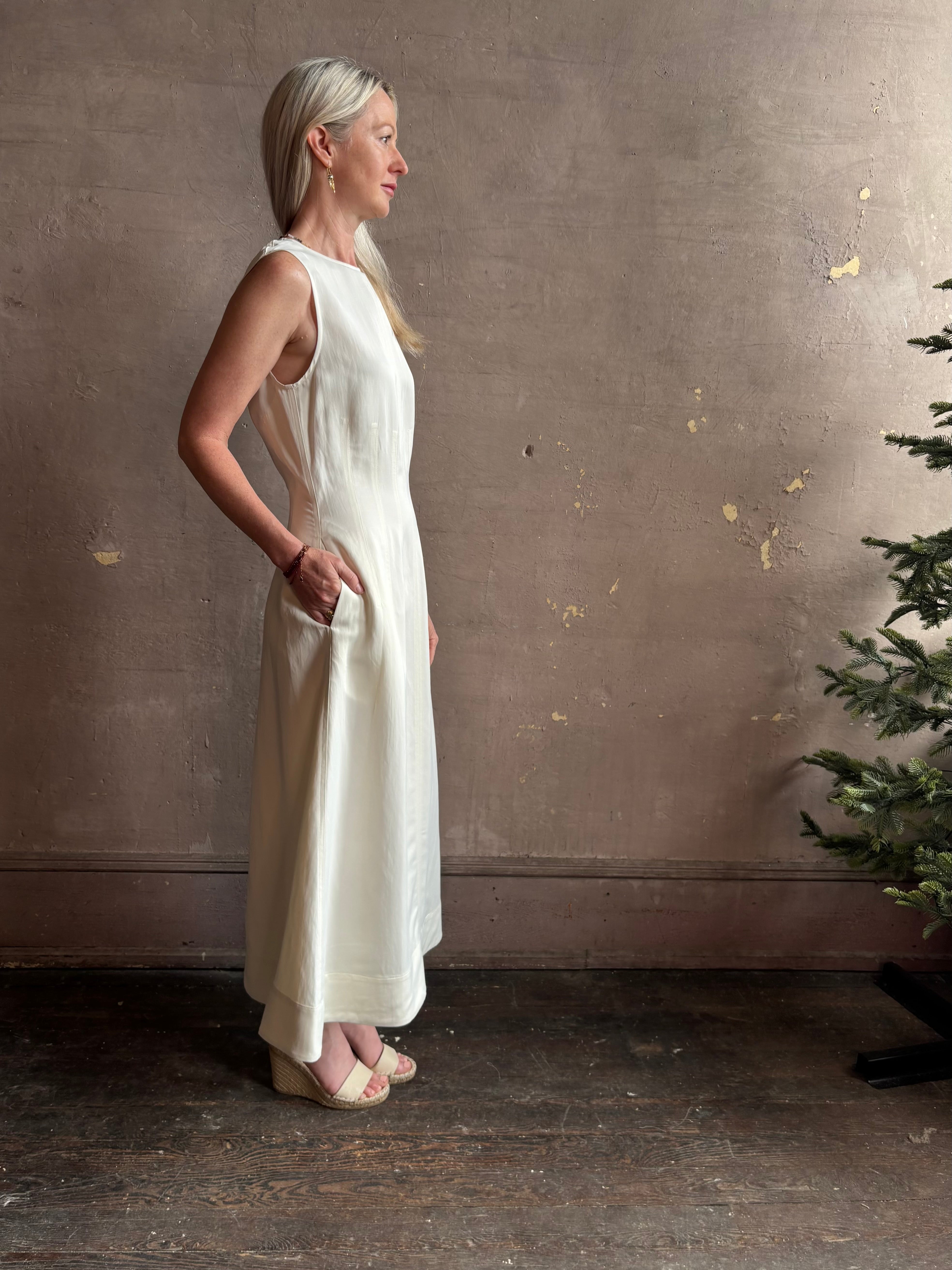 Mature woman wearing elegant Crew Neck maxi A-Line Dress with Darts from TWP rendered in a soft off white and crafted in the USA from a viscose and linen fabric blend with side seam pockets and sleeveless
