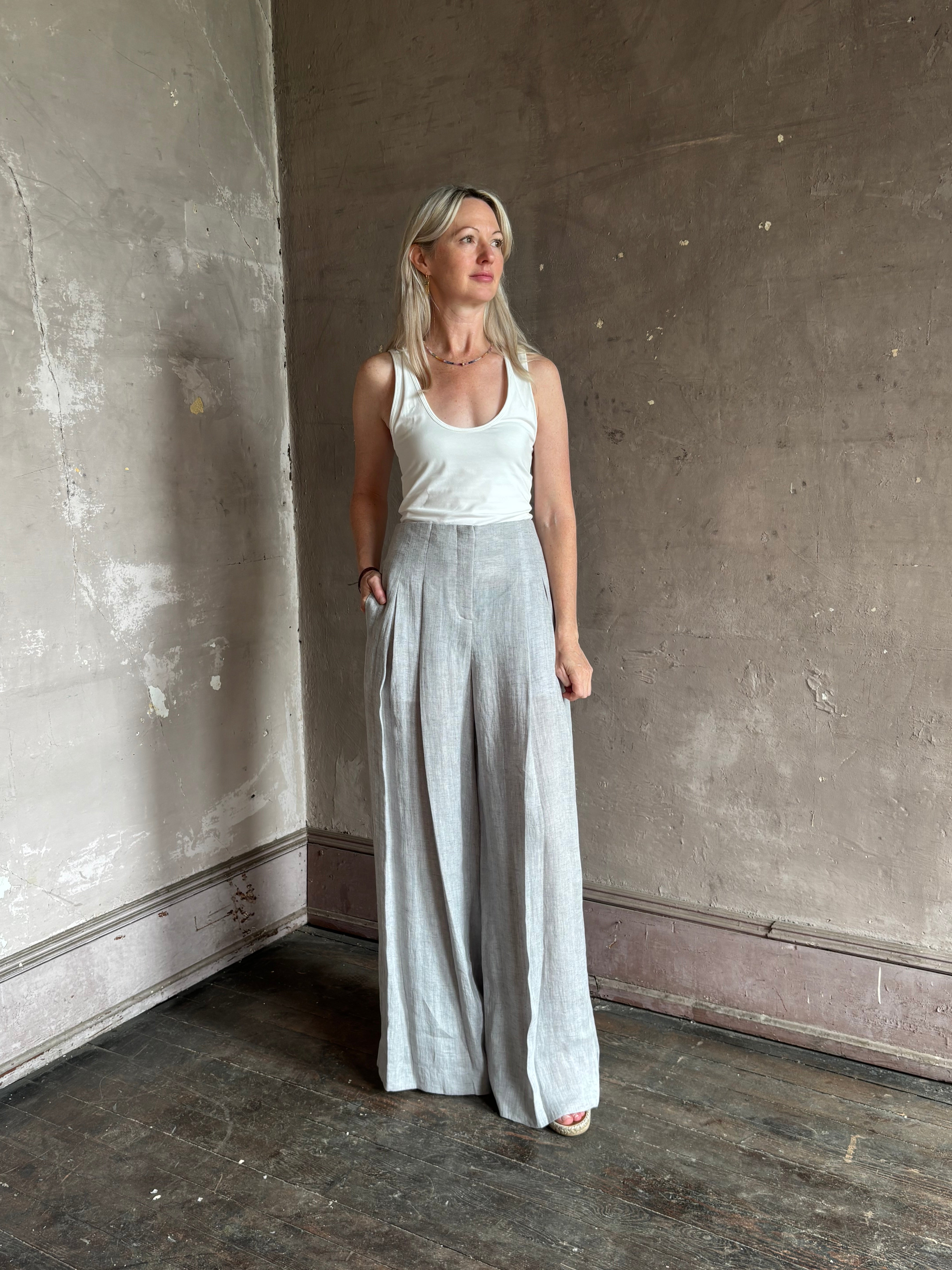 Mature woman wearing effortless women's designer Drew wide leg Trouser from TWP rendered in a versatile light heather grey and crafted from light weight hemp with high-rise, drop waist pleats, and side seam pockets, and made in the USA