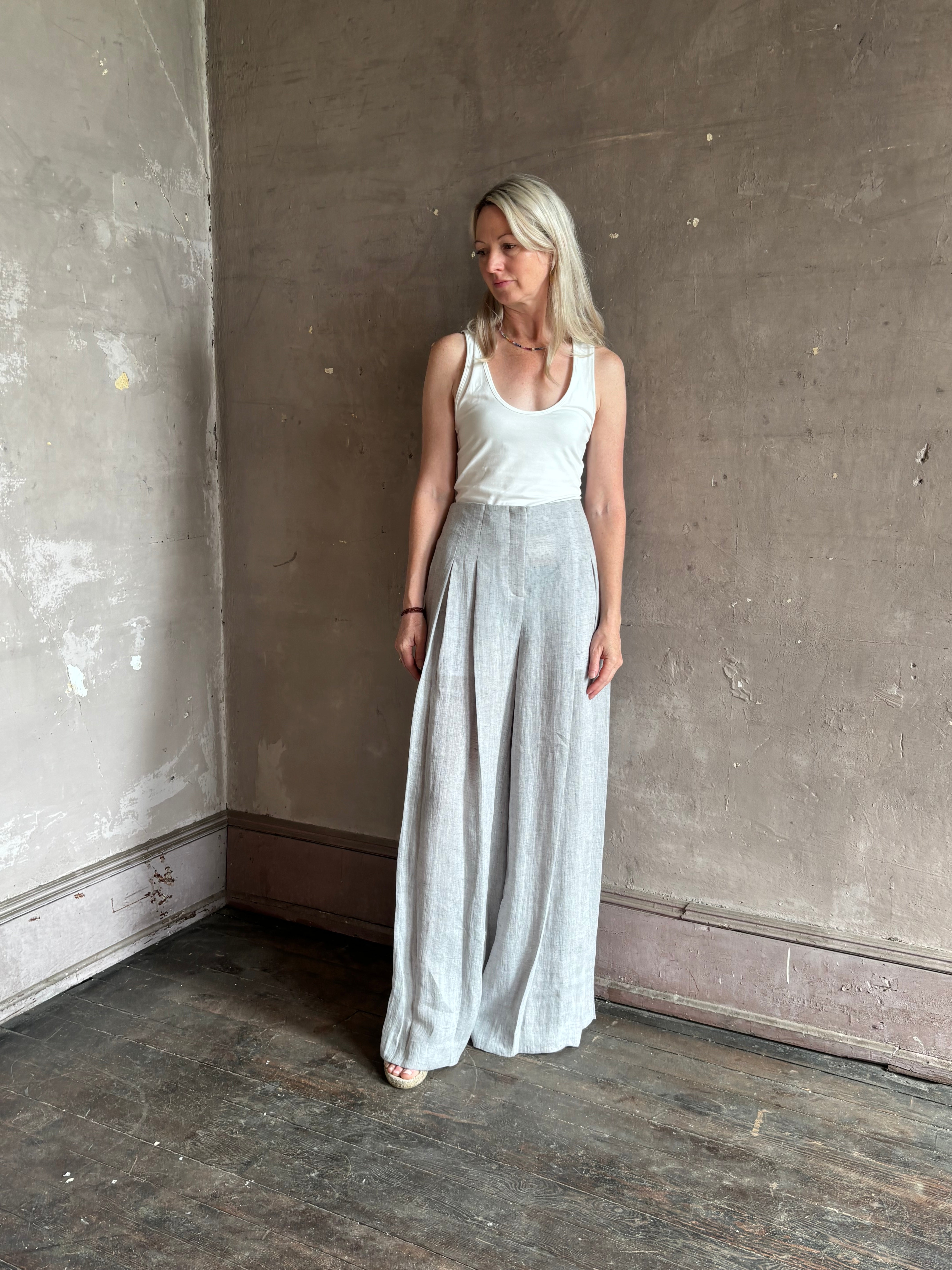 Mature woman wearing effortless women's designer Drew wide leg Trouser from TWP rendered in a versatile light heather grey and crafted from light weight hemp with high-rise, drop waist pleats, and side seam pockets, and made in the USA