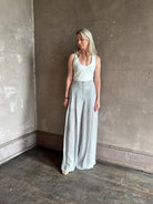 Mature woman wearing effortless women's designer Drew wide leg Trouser from TWP rendered in a versatile light heather grey and crafted from light weight hemp with high-rise, drop waist pleats, and side seam pockets, and made in the USA