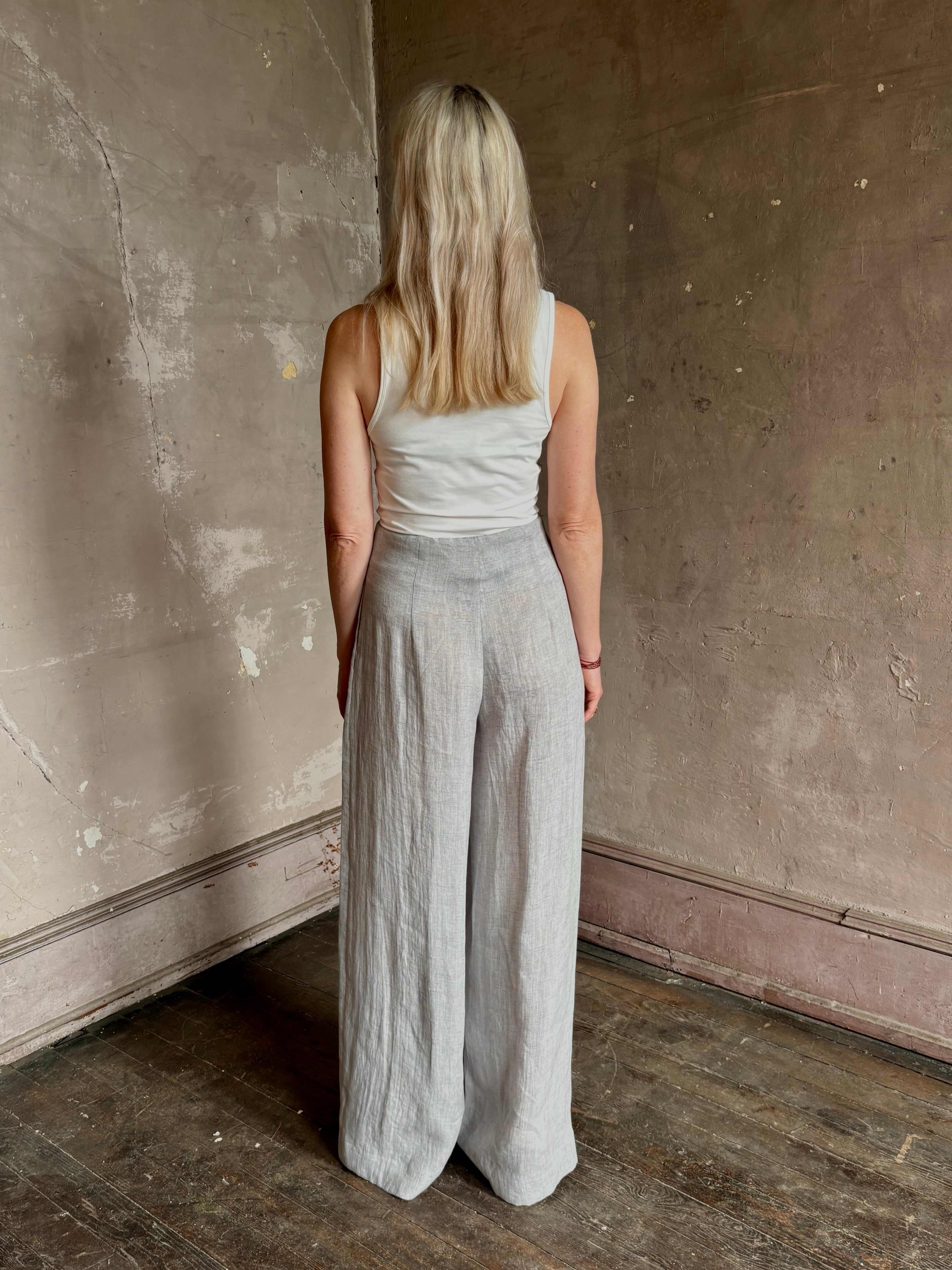 Mature woman wearing effortless women's designer Drew wide leg Trouser from TWP rendered in a versatile light heather grey and crafted from light weight hemp with high-rise, drop waist pleats, and side seam pockets, and made in the USA
