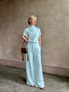 Mature woman wearing the Dylan Pant from TWP rendered in a sea glass blue hue and crafted from a viscose and linen blend, made in the USA, this luxury mid-rise trouser offers a wide leg silhouette with hidden seam side and back pockets 