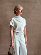 Mature woman wearing the Dylan Pant from TWP rendered in a sea glass blue hue and crafted from a viscose and linen blend, made in the USA, this luxury mid-rise trouser offers a wide leg silhouette with hidden seam side and back pockets 