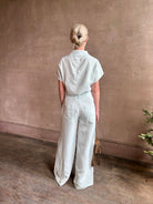 Mature woman wearing the Dylan Pant from TWP rendered in a sea glass blue hue and crafted from a viscose and linen blend, made in the USA, this luxury mid-rise trouser offers a wide leg silhouette with hidden seam side and back pockets 