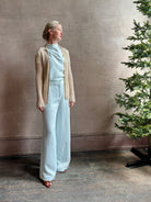 Mature woman wearing the Dylan Pant from TWP rendered in a sea glass blue hue and crafted from a viscose and linen blend, made in the USA, this luxury mid-rise trouser offers a wide leg silhouette with hidden seam side and back pockets 