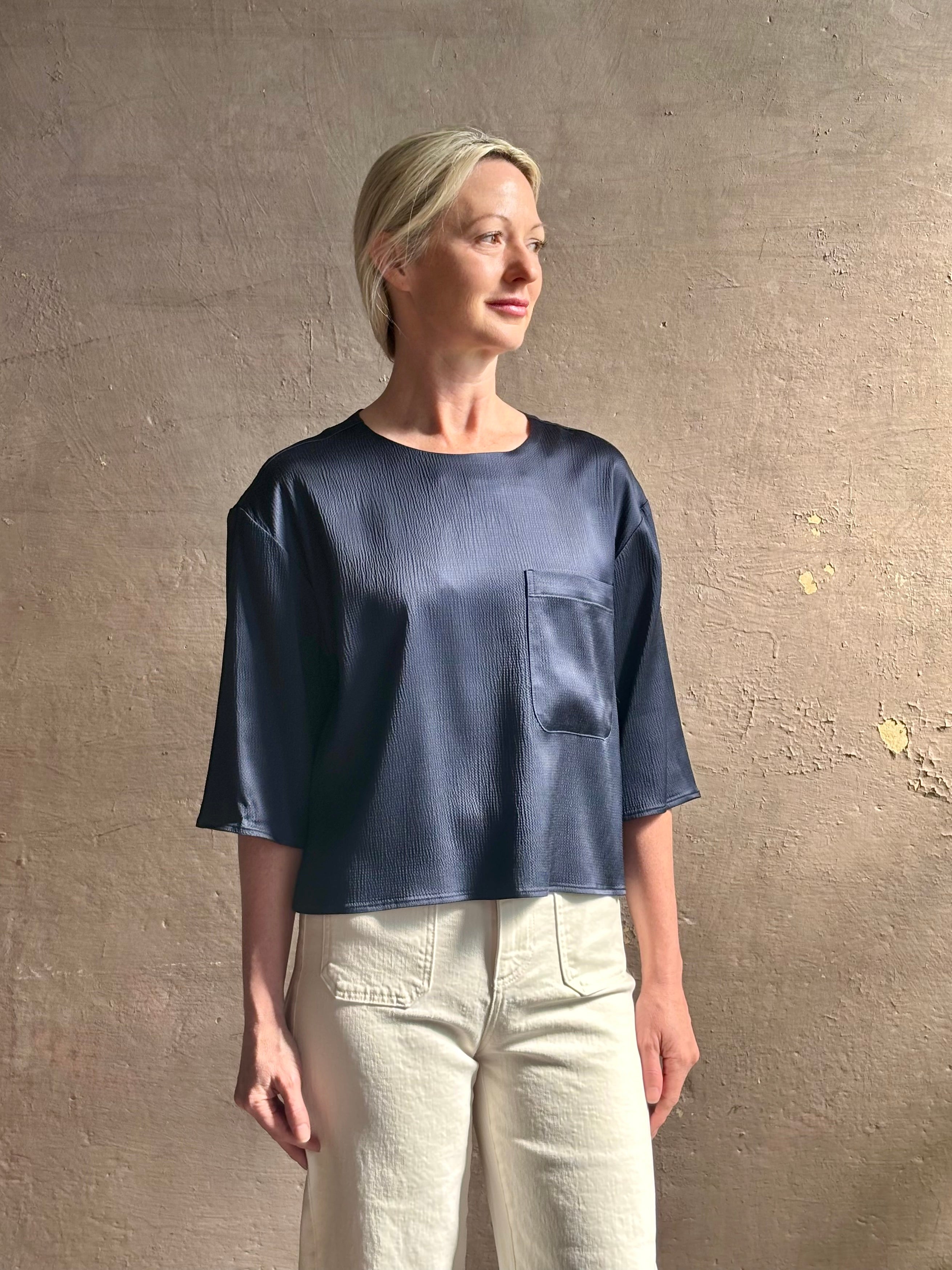 Mature woman wearing Women's luxury  clothing brand TWP Ex T in premium hammered satin with short sleeves crew neck and a casual front pocket rendered in a beautiful navy blue hue