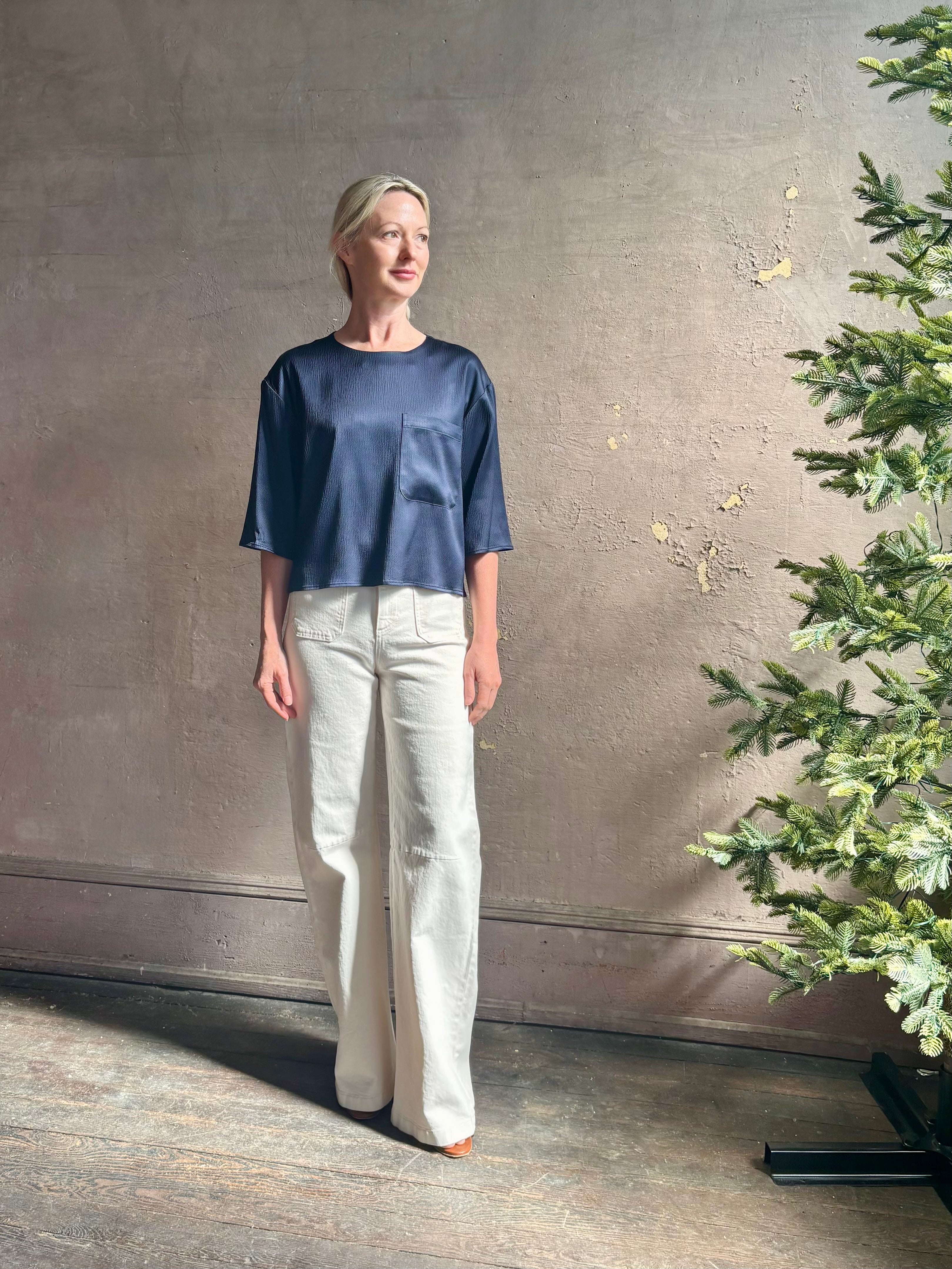 Mature woman wearing Women's luxury  clothing brand TWP Ex T in premium hammered satin with short sleeves crew neck and a casual front pocket rendered in a beautiful navy blue hue