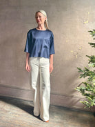 Mature woman wearing Women's luxury  clothing brand TWP Ex T in premium hammered satin with short sleeves crew neck and a casual front pocket rendered in a beautiful navy blue hue
