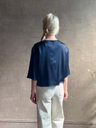 Mature woman wearing Women's luxury  clothing brand TWP Ex T in premium hammered satin with short sleeves crew neck and a casual front pocket rendered in a beautiful navy blue hue