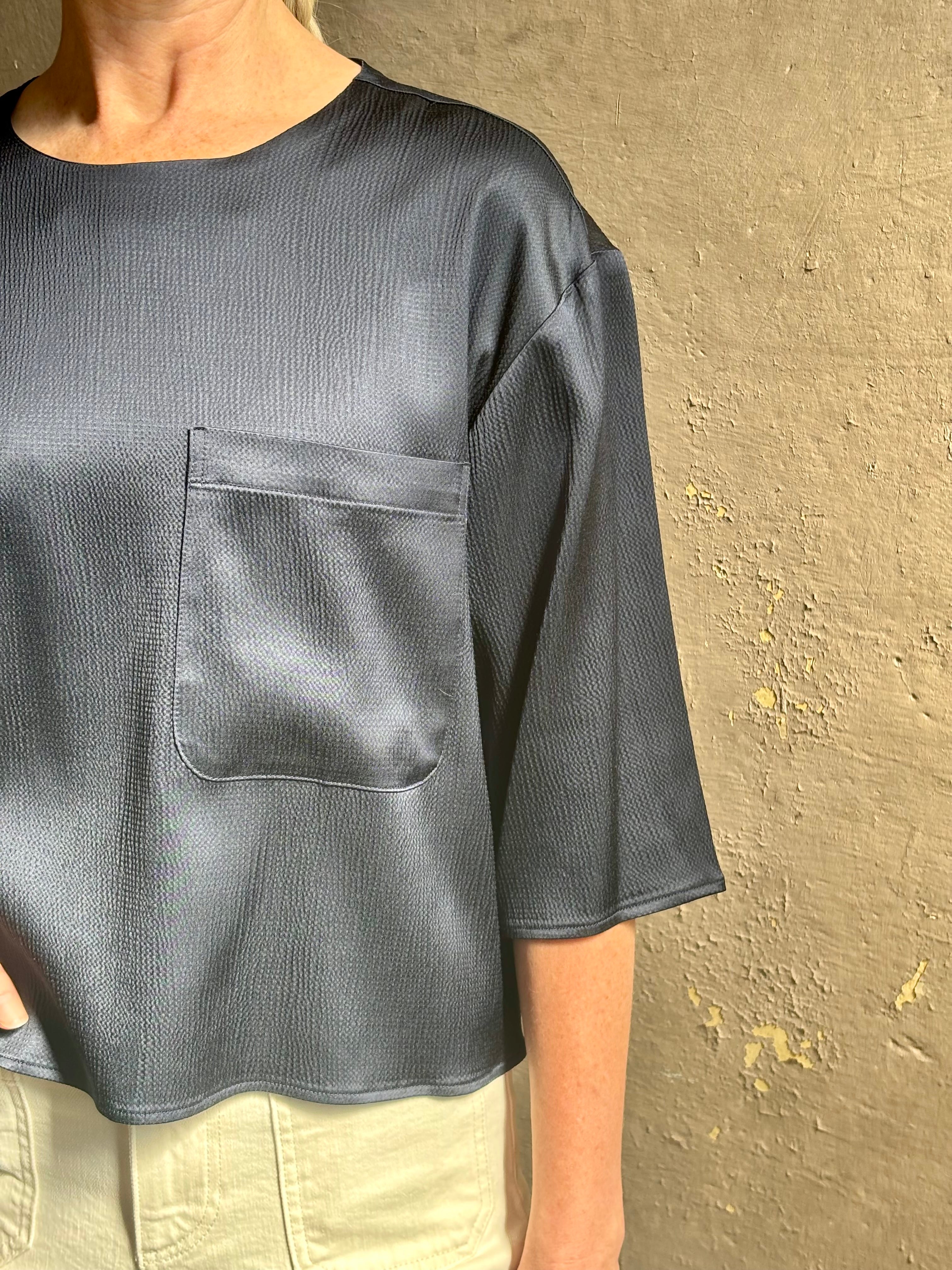 Mature woman wearing Women's luxury  clothing brand TWP Ex T in premium hammered satin with short sleeves crew neck and a casual front pocket rendered in a beautiful navy blue hue