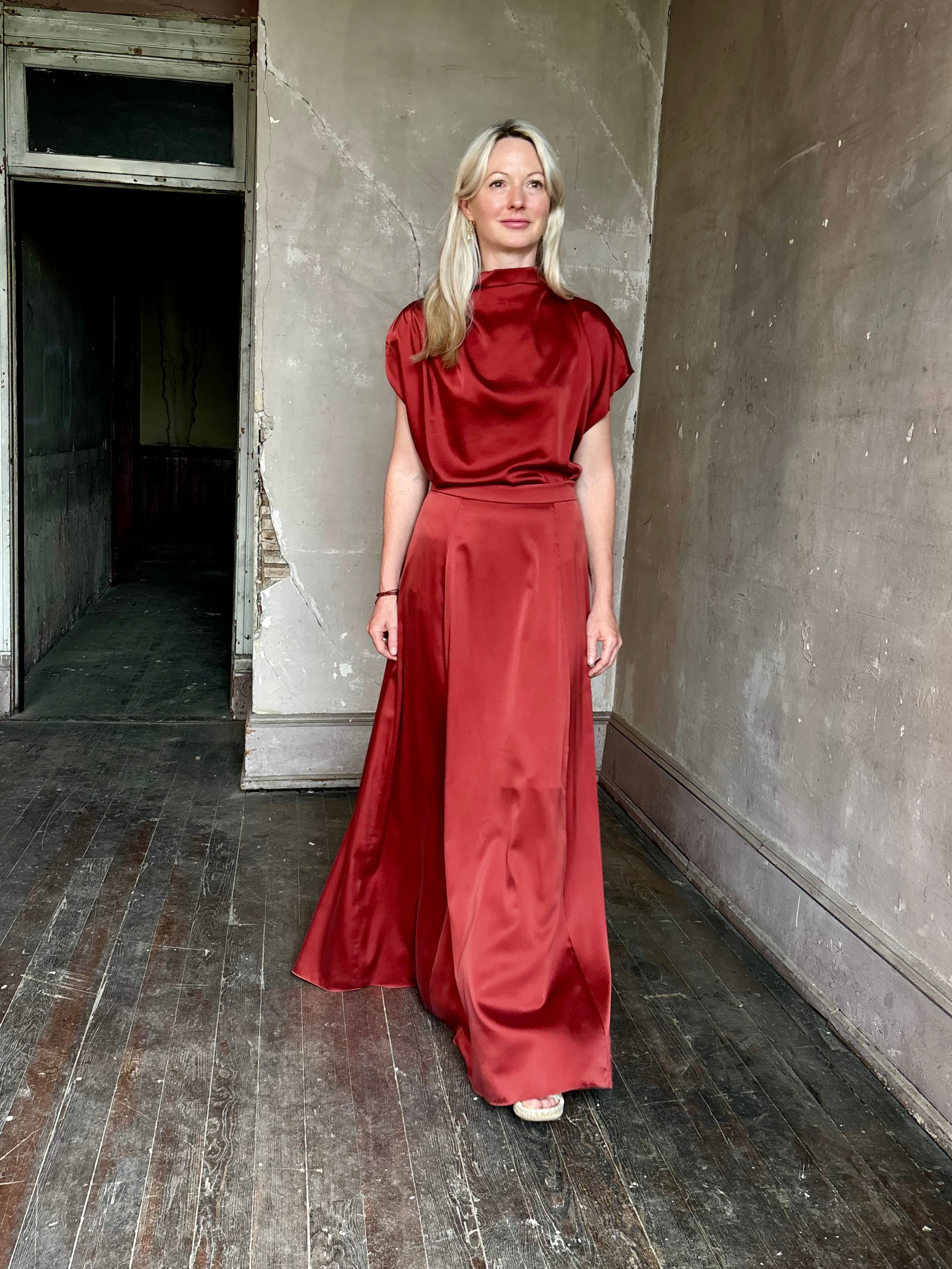 Mature woman wearing Flowy Maxi A-Line Skirt from TWP rendered in a rich red currant and crafted from a luxurious  silk blend with hidden seam zip closure and tailored waistband