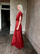 Mature woman wearing Flowy Maxi A-Line Skirt from TWP rendered in a rich red currant and crafted from a luxurious  silk blend with hidden seam zip closure and tailored waistband