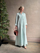 Mature woman wearing floor-length Jenny's Gown from TWP rendered in a sea glass hue and crafted from a viscose linen blend with beautiful draping, long sleeves, button front and cool girl loose fit