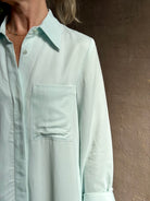 Mature woman wearing floor-length Jenny's Gown from TWP rendered in a sea glass hue and crafted from a viscose linen blend with beautiful draping, long sleeves, button front and cool girl loose fit