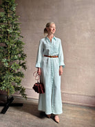Mature woman wearing floor-length Jenny's Gown from TWP rendered in a sea glass hue and crafted from a viscose linen blend with beautiful draping, long sleeves, button front and cool girl loose fit