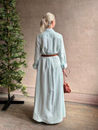 Mature woman wearing floor-length Jenny's Gown from TWP rendered in a sea glass hue and crafted from a viscose linen blend with beautiful draping, long sleeves, button front and cool girl loose fit