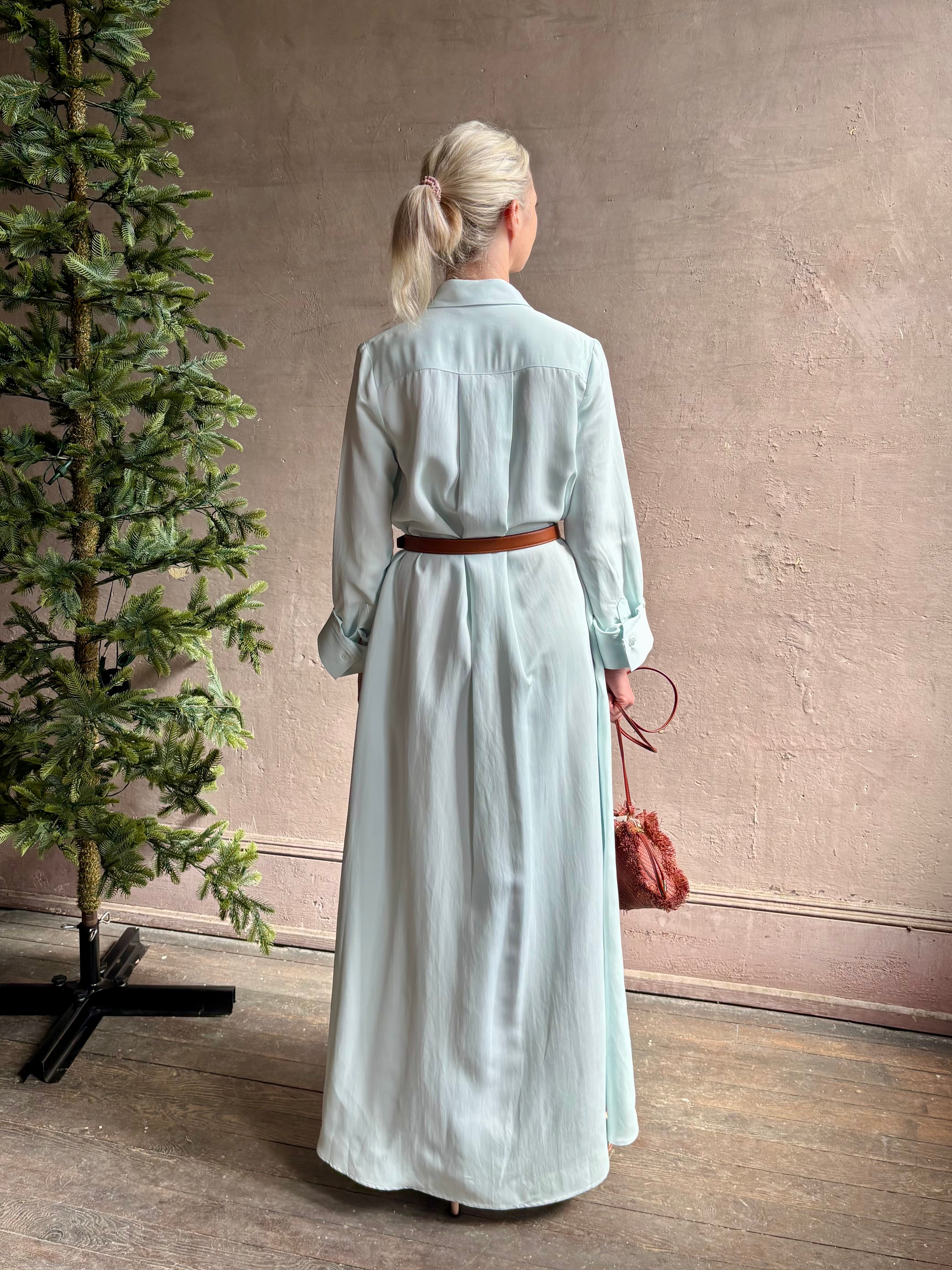 Mature woman wearing floor-length Jenny's Gown from TWP rendered in a sea glass hue and crafted from a viscose linen blend with beautiful draping, long sleeves, button front and cool girl loose fit