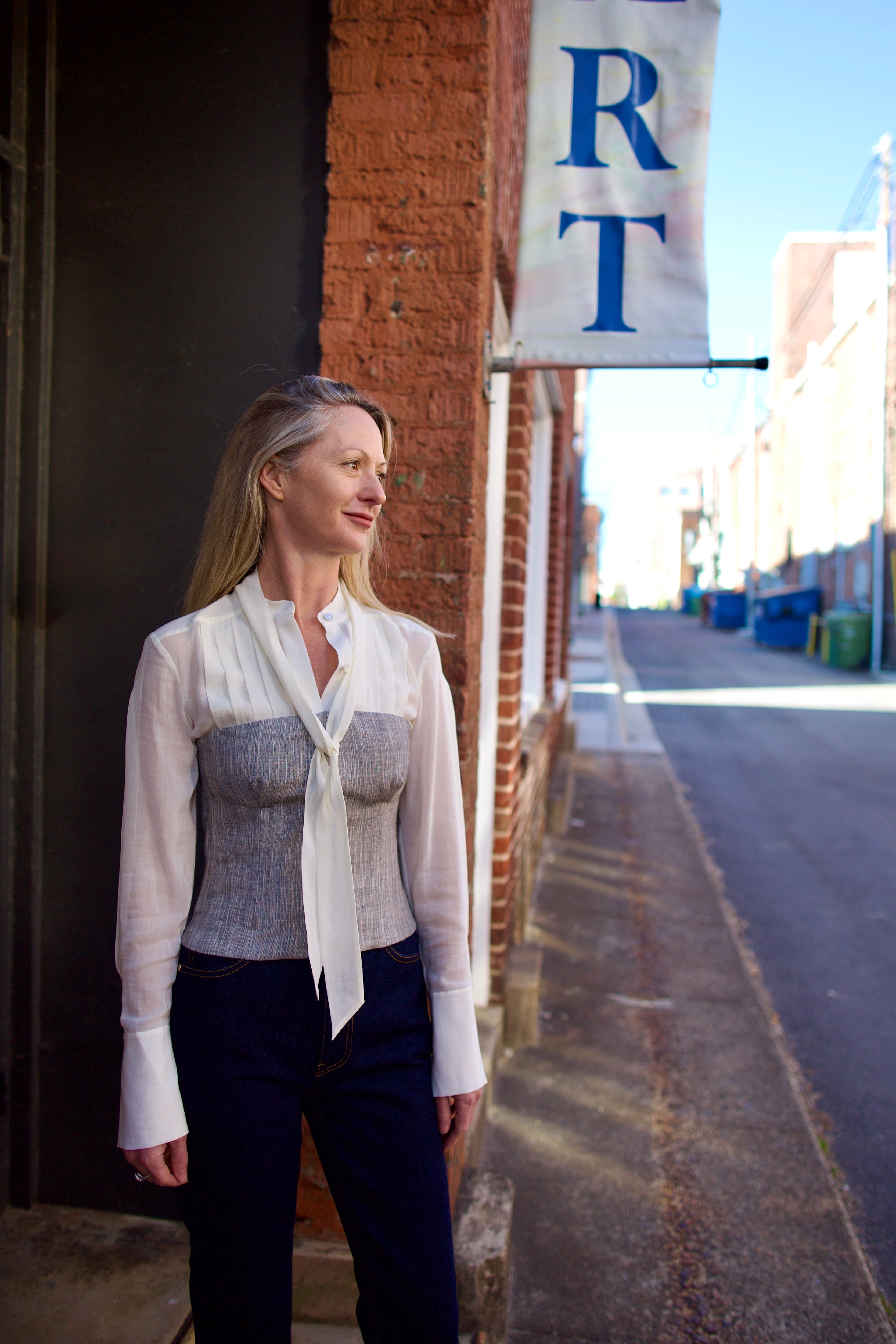 Mature woman wearing luxury brand TWP Jillian cotton-wool bustier in heather grey with bust darts zip closure over long sleeve blouse
