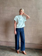 Mature woman wearing refined Mock Neck Tee Blouse from TWP rendered in a subtle sea glass blue hue and crafted from a viscose linen blend made in the USA, with short sleeves, asymmetrical design and quality fabric draping