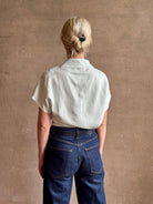 Mature woman wearing refined Mock Neck Tee Blouse from TWP rendered in a subtle sea glass blue hue and crafted from a viscose linen blend made in the USA, with short sleeves, asymmetrical design and quality fabric draping