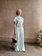 Mature woman wearing refined Mock Neck Tee Blouse from TWP rendered in a subtle sea glass blue hue and crafted from a viscose linen blend made in the USA, with short sleeves, asymmetrical design and quality fabric draping