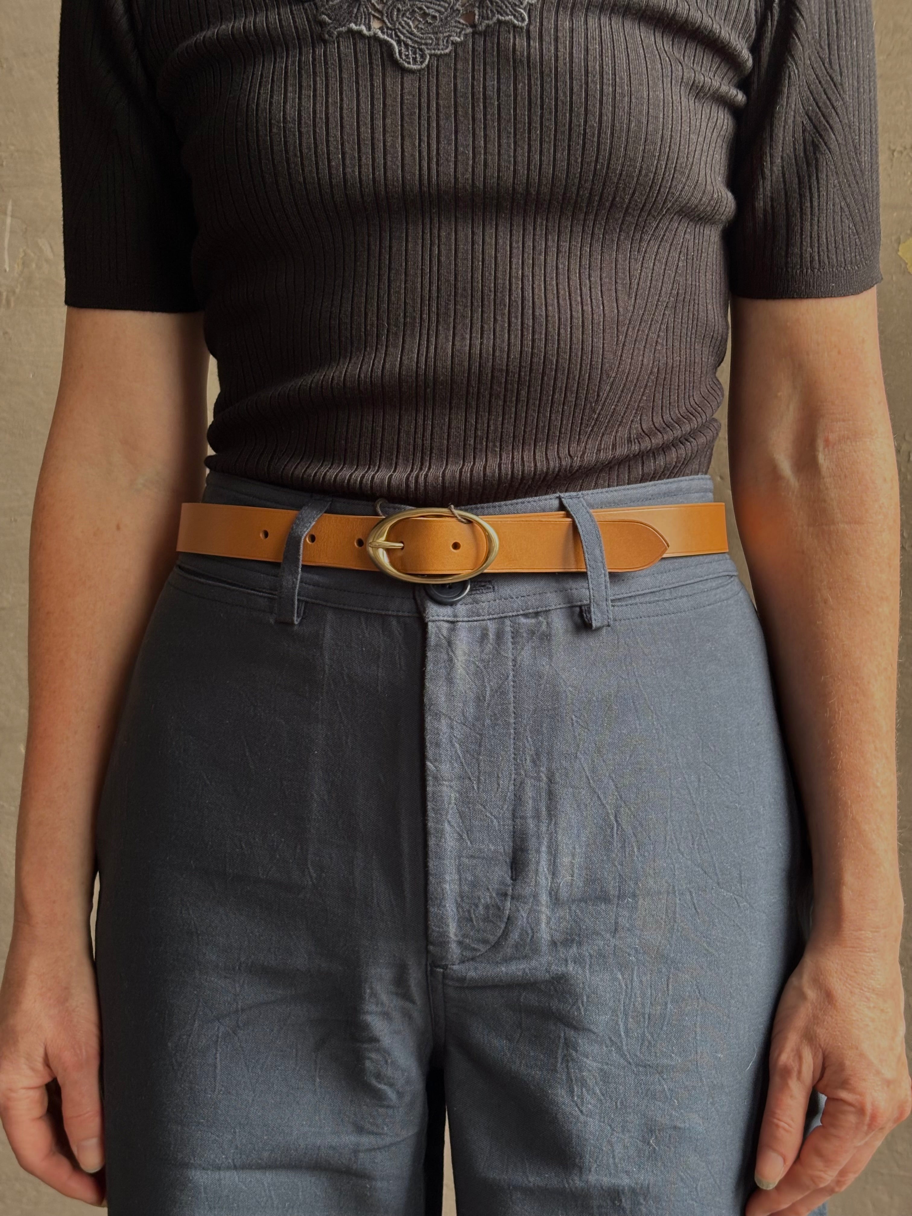 Mature woman wearing a TWP vintage camel brown narrow leather belt with warm gold tone oval buckle