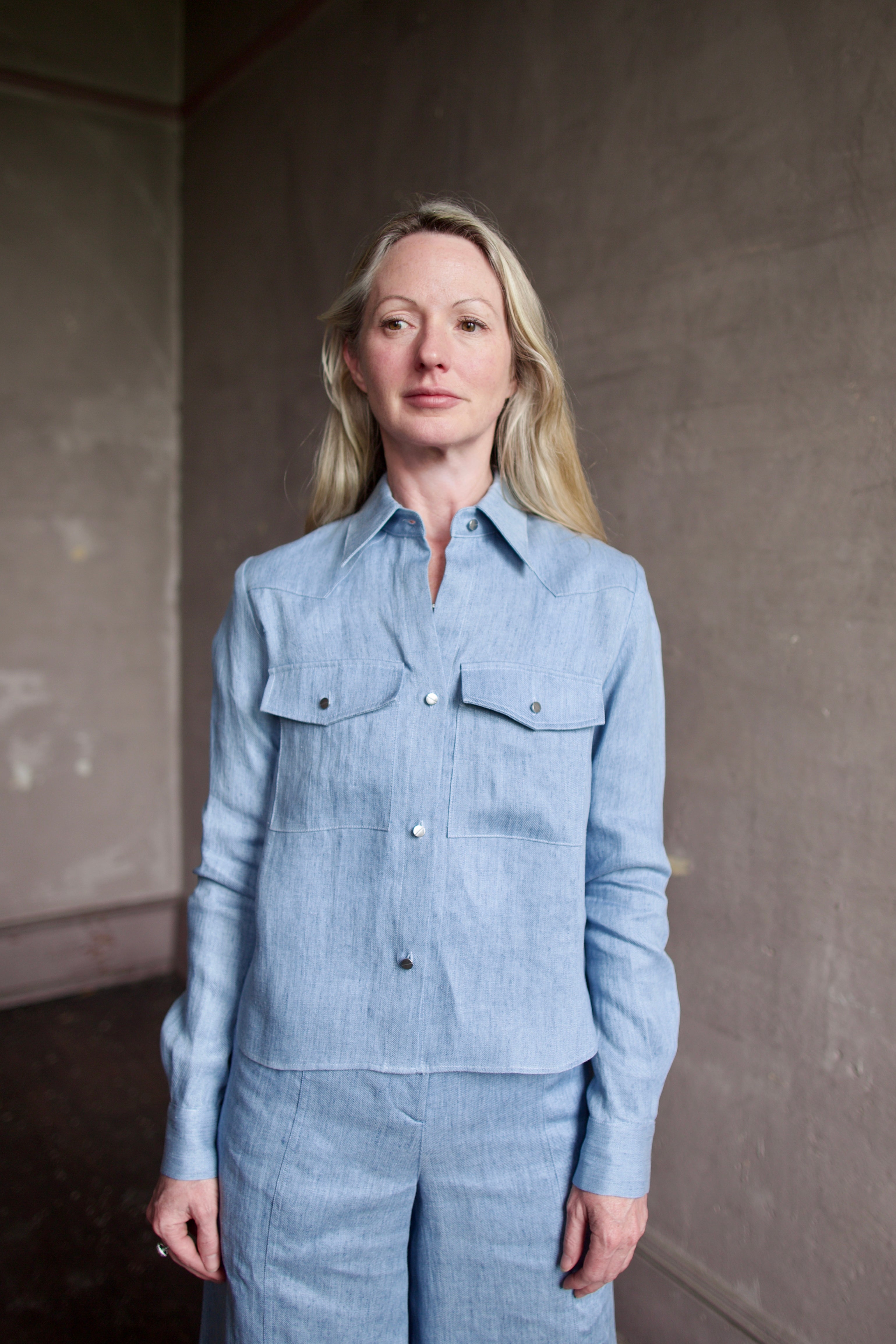 Mature woman wearing luxury TWP New Carter indigo Button Up hemp top combining timeless workwear with contemporary refinement with long sleeves, metal buttons, collar and front pockets